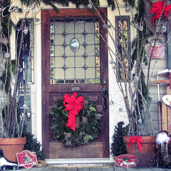 Fascinating Front Porch Decorating For Christmas By Green Circle With Red Ribbon Placed On The Brown Wooden Door Between Brown Pot With Sticks